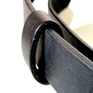 K&ouml;nnte beinhalten: Nahaufnahme eines schwarzen Lederg&uuml;rtels mit strukturierter Oberfl&auml;che. Der G&uuml;rtel ist durch eine passende schwarze G&uuml;rtelschlaufe geschlungen, wodurch ein schlankes und minimalistisches Design entsteht. Das Bild hebt das Material und die Konstruktion des G&uuml;rtels hervor.