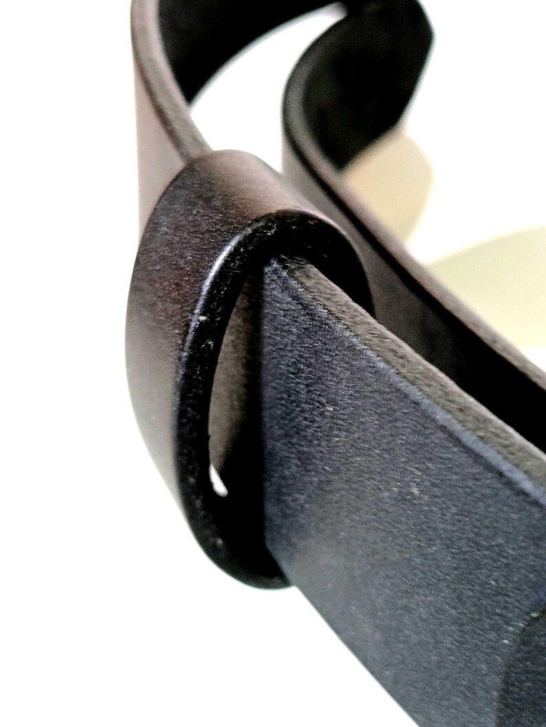 K&ouml;nnte beinhalten: Nahaufnahme eines schwarzen Lederg&uuml;rtels mit strukturierter Oberfl&auml;che. Der G&uuml;rtel ist durch eine passende schwarze G&uuml;rtelschlaufe geschlungen, wodurch ein schlankes und minimalistisches Design entsteht. Das Bild hebt das Material und die Konstruktion des G&uuml;rtels hervor.