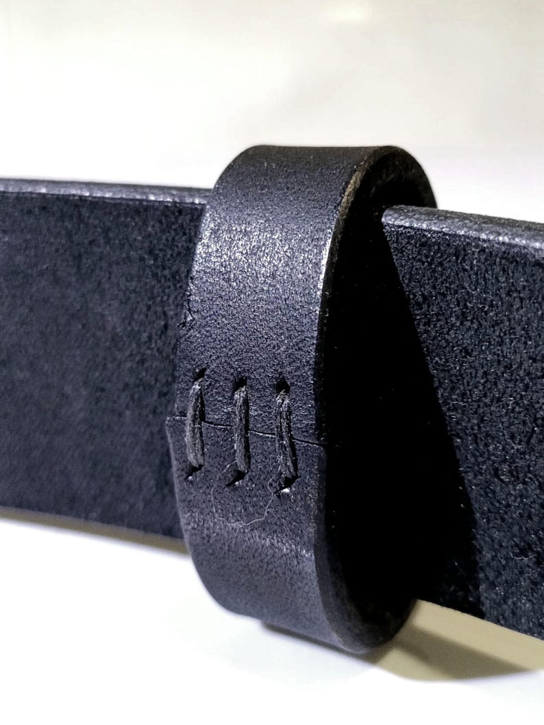 Op de afbeelding: Close-up van een zwarte leren riem met een getextureerd oppervlak. De riemlus is ook zwart en heeft drie verticale steken. Het leer lijkt dik en duurzaam, geschikt voor dagelijks gebruik.