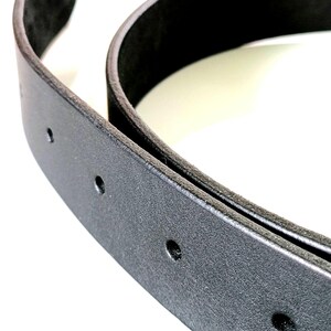 K&ouml;nnte beinhalten: Nahaufnahme eines schwarzen Lederg&uuml;rtels mit mehreren gleichm&auml;&szlig;ig verteilten L&ouml;chern. Der G&uuml;rtel ist gebogen und zeigt seine Dicke und Textur. Der Hintergrund ist wei&szlig; und hebt die Details des G&uuml;rtels hervor.