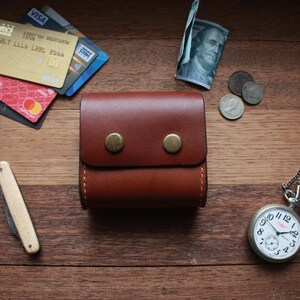 May include: A brown leather wallet with two brass snaps and a pocket watch with a silver chain on a wooden surface.