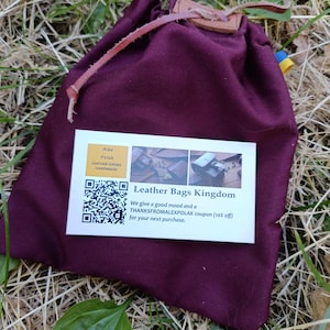 Puede incluir: Una bolsa de tela de color morado oscuro con cierre de cord&oacute;n, una leng&uuml;eta de cuero y un cord&oacute;n. En la parte frontal hay una tarjeta de visita rectangular blanca con un c&oacute;digo QR, el texto Leather Bags Kingdom y un cup&oacute;n de descuento.