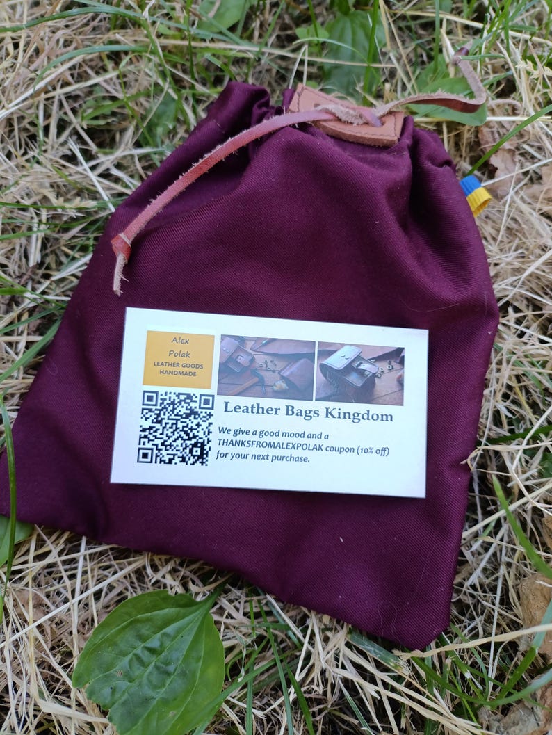 Puede incluir: Una bolsa de tela de color morado oscuro con cierre de cord&oacute;n, una leng&uuml;eta de cuero y un cord&oacute;n. En la parte frontal hay una tarjeta de visita rectangular blanca con un c&oacute;digo QR, el texto Leather Bags Kingdom y un cup&oacute;n de descuento.