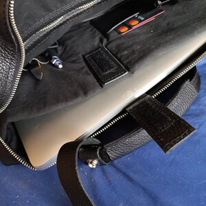 Puede incluir: Bolso para port&aacute;til de cuero negro con cremallera plateada y asa. El bolso est&aacute; abierto, revelando un port&aacute;til en el interior, junto con un peque&ntilde;o bolsillo que contiene una tarjeta de cr&eacute;dito. El interior es negro.