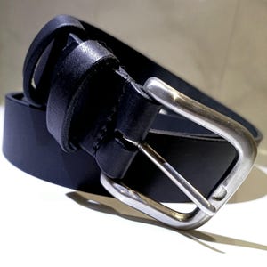 Op de afbeelding: Een zwarte leren riem met een zilverkleurige gesp. De riem is gemaakt van glad, donker leer en heeft een klassieke rechthoekige gesp. De riem is ontworpen voor dagelijks gebruik en is een veelzijdig accessoire.