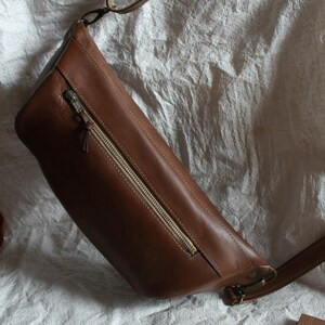 May include: A brown leather crossbody bag with a zipper closure and a long adjustable strap.