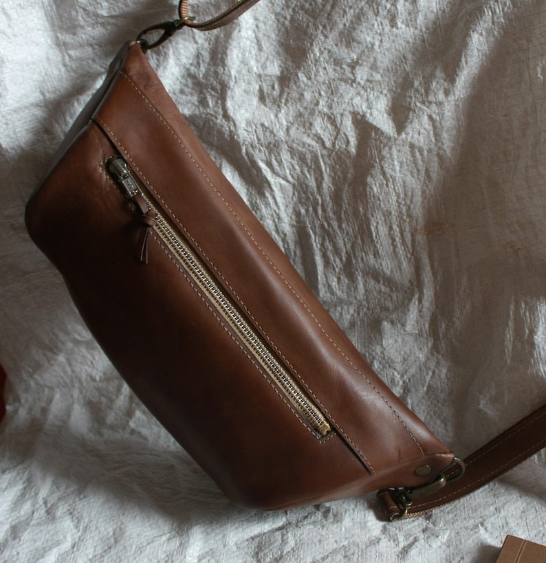 May include: A brown leather crossbody bag with a zipper closure and a long adjustable strap.