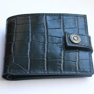 May include: Black leather wallet with a crocodile embossed pattern and a snap closure. The snap has a metal button with the text "Classic New Fashion" engraved on it.