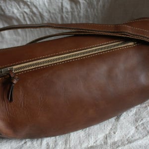 May include: A brown leather bag with a zipper closure and a strap. The bag is made of a soft, supple leather and has a classic, timeless design.