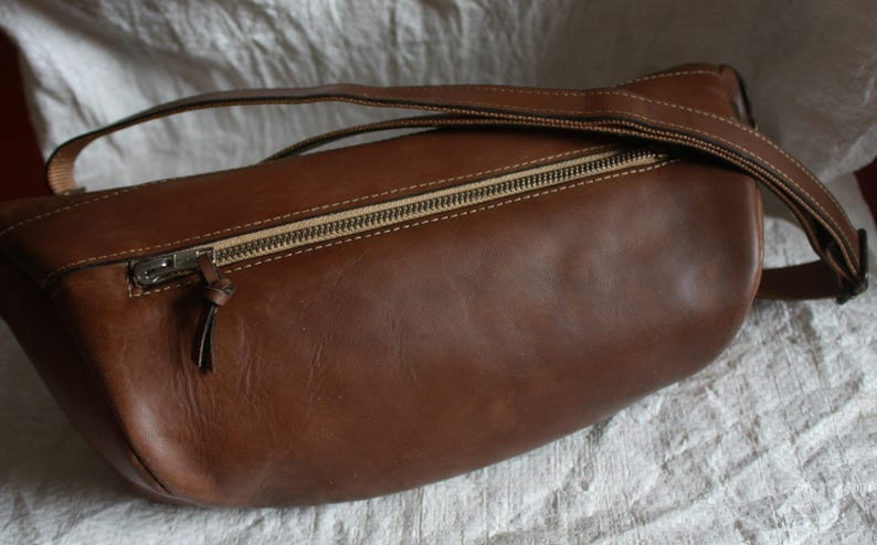 May include: A brown leather bag with a zipper closure and a strap. The bag is made of a soft, supple leather and has a classic, timeless design.