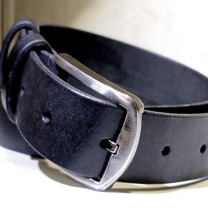 May include: A close-up of a black leather belt with a silver buckle. The belt is curved, showing the texture of the leather and the details of the buckle's design. The buckle is a classic, rectangular shape.