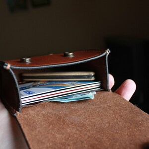 May include: A brown leather wallet with a flap closure, open to reveal a stack of credit cards and cash inside.