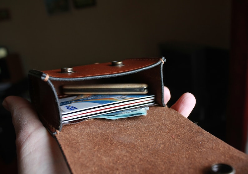May include: A brown leather wallet with a flap closure, open to reveal a stack of credit cards and cash inside.