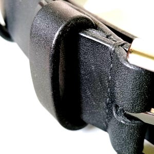 K&ouml;nnte beinhalten: Nahaufnahme eines schwarzen Lederg&uuml;rtels mit einer silbernen Schnalle. Der G&uuml;rtel besteht aus einem strukturierten Material und hat ein klassisches Design. Die Schnalle ist silberfarben gl&auml;nzend.