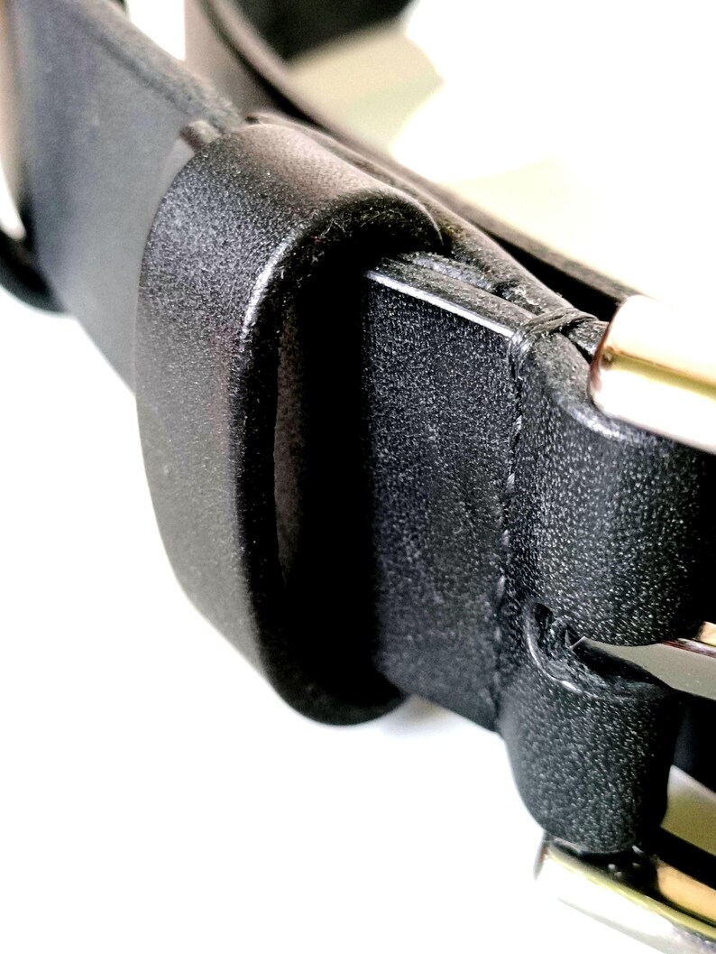 K&ouml;nnte beinhalten: Nahaufnahme eines schwarzen Lederg&uuml;rtels mit einer silbernen Schnalle. Der G&uuml;rtel besteht aus einem strukturierten Material und hat ein klassisches Design. Die Schnalle ist silberfarben gl&auml;nzend.