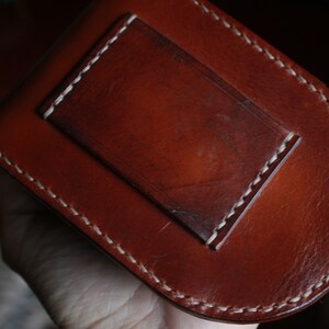 May include: A brown leather wallet with a white stitched border and a smaller pocket on the front.