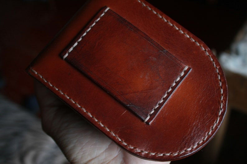 May include: A brown leather wallet with a white stitched border and a smaller pocket on the front.