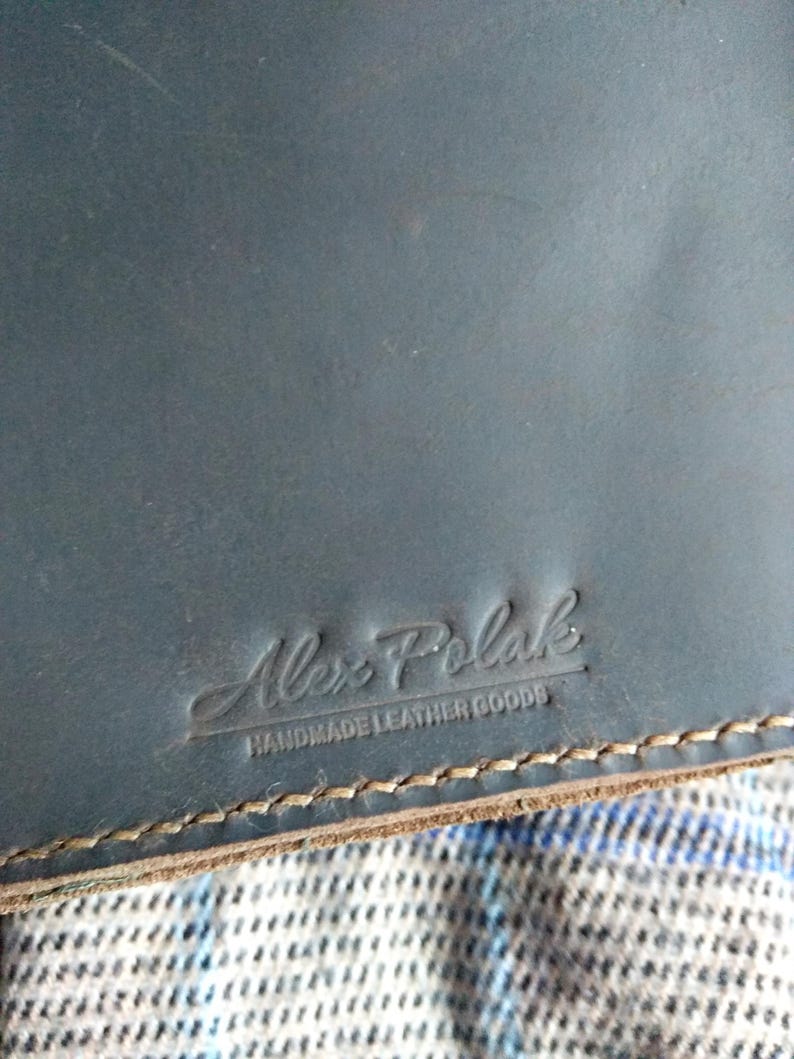 Pu&ograve; includere: Un taccuino in pelle blu scuro con il testo "Alex Polak Handmade Leather Goods" in rilievo sulla copertina.