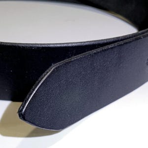 May include: Close-up of a black leather belt. The belt is made of a smooth, dark material and has a classic design. The buckle is not visible in the image.