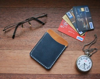 May include: A blue leather card holder with a tan leather accent, a silver pocket watch with a chain, and a stack of credit cards with the VISA logo.