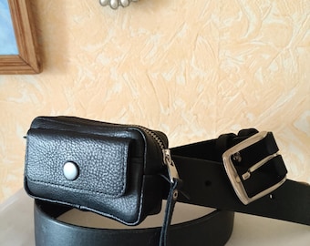 Könnte beinhalten: Ein schwarzer Ledergürtel mit einer rechteckigen Tasche, die am Riemen befestigt ist. Die Tasche hat eine Klappe mit einem silberfarbenen Druckknopf und einen seitlichen Reißverschluss. Der Gürtelriemen ist glatt mit einer silbernen Metallschnalle.