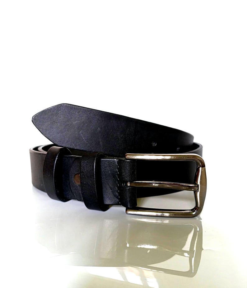 K&ouml;nnte beinhalten: Ein schwarzer Lederg&uuml;rtel mit einer silberfarbenen Schnalle. Der G&uuml;rtel besteht aus einem einzigen Lederst&uuml;ck und hat ein klassisches Design. Die Schnalle ist rechteckig und hat ein schlichtes, elegantes Aussehen.