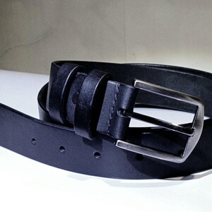 May include: A black leather belt with a silver buckle. The belt is rolled up, showing the buckle and the belt holes. The leather appears smooth and the belt is a classic style.