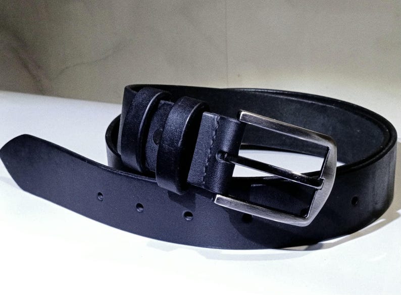 May include: A black leather belt with a silver buckle. The belt is rolled up, showing the buckle and the belt holes. The leather appears smooth and the belt is a classic style.