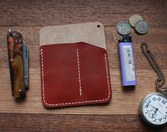 May include: A brown leather wallet with two pockets and white stitching. The wallet is on a wooden surface with a pocket knife, a lighter, coins, and a pocket watch.