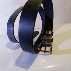 May include: A black leather belt with a silver buckle. The belt is looped, showing the front and back of the leather. The belt has two holes for adjustment.