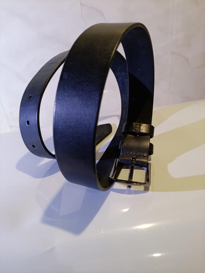 May include: A black leather belt with a silver buckle. The belt is looped, showing the front and back of the leather. The belt has two holes for adjustment.