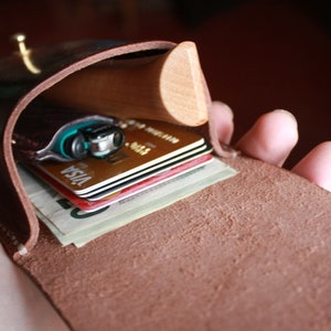 May include: A brown leather wallet with a wooden accent, open to reveal a lighter, credit cards, and folded bills. The wallet is held open, showcasing its contents. The leather has a natural, textured appearance.