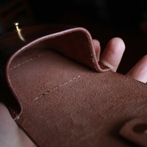 May include: A brown leather case with a stitched seam and a flap that folds over. The case is open and the inside is visible.