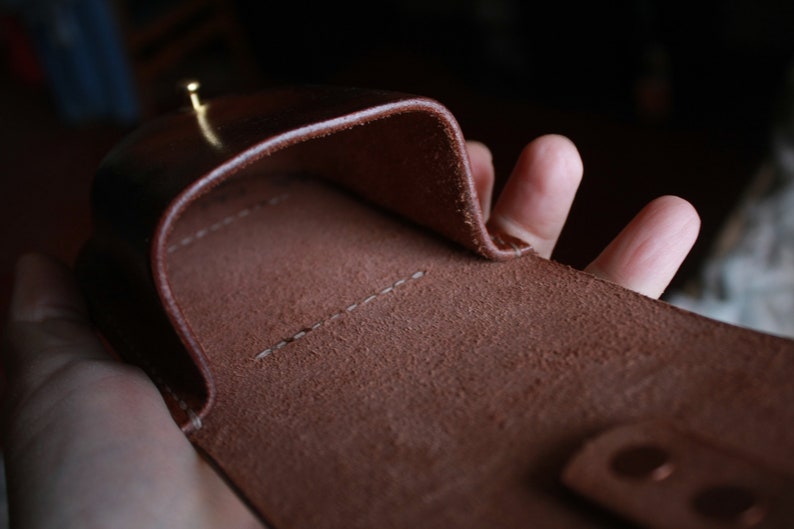 May include: A brown leather case with a stitched seam and a flap that folds over. The case is open and the inside is visible.