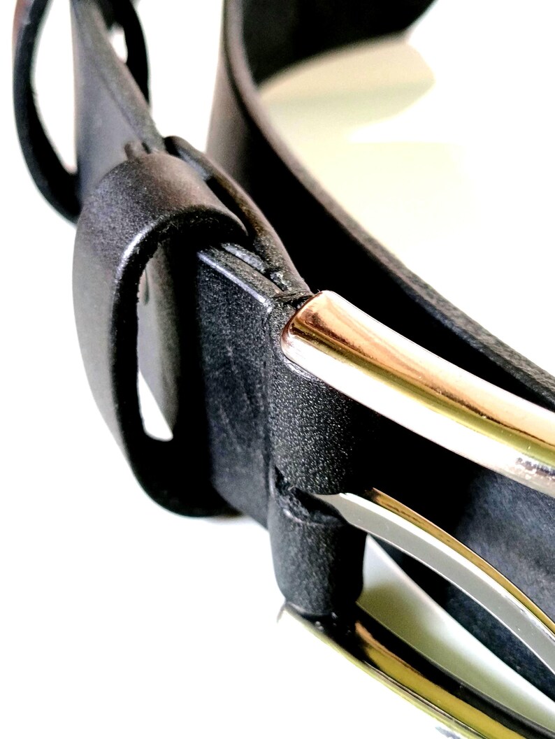 K&ouml;nnte beinhalten: Nahaufnahme eines schwarzen Lederg&uuml;rtels mit goldfarbener Schnalle. Der G&uuml;rtel hat eine strukturierte Oberfl&auml;che und ein klassisches Design. Die Schnalle ist rechteckig und hat ein gl&auml;nzendes Finish. Der G&uuml;rtel ist wahrscheinlich f&uuml;r Hosen.