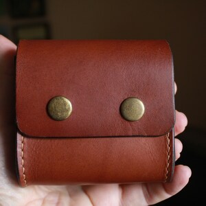 May include: A brown leather wallet with two brass snaps. The wallet has a fold-over flap and a stitched edge.