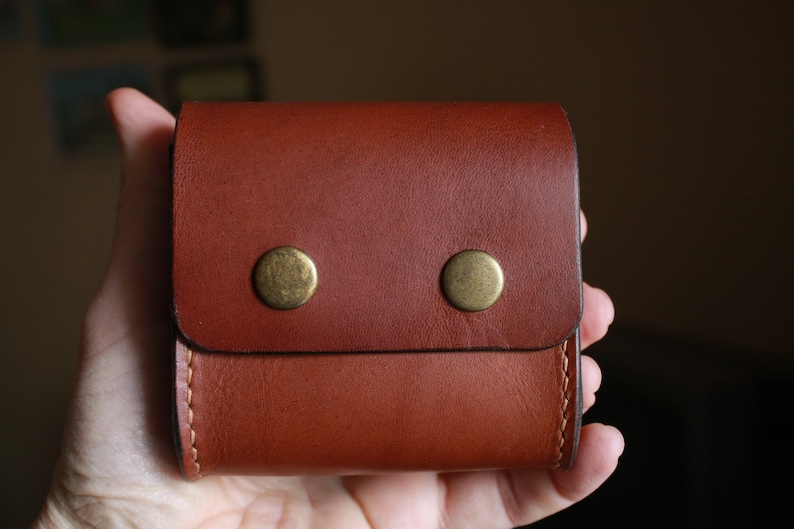 May include: A brown leather wallet with two brass snaps. The wallet has a fold-over flap and a stitched edge.