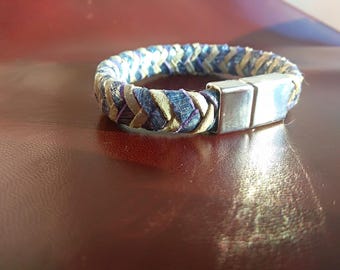 Puede incluir: Un brazalete de cuero trenzado con un cierre plateado. El brazalete está hecho de cuero azul y beige y tiene un patrón tejido.