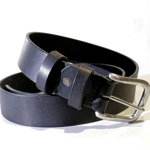 Op de afbeelding: Een zwarte leren riem met een zilverkleurige gesp. De riem is opgerold, wat de textuur van het leer en de details van de gesp laat zien. Een klassiek accessoire voor broeken.