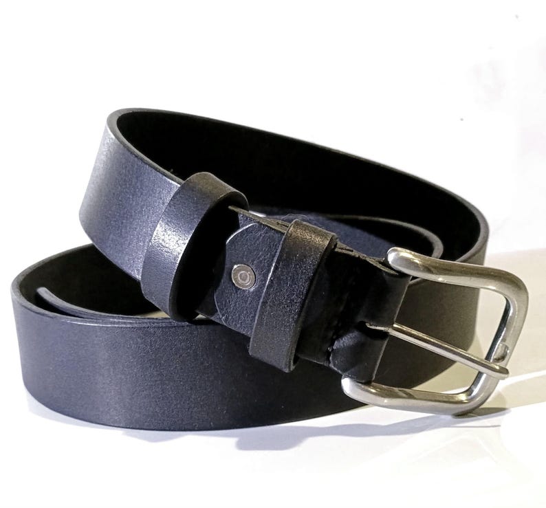 Op de afbeelding: Een zwarte leren riem met een zilverkleurige gesp. De riem is opgerold, wat de textuur van het leer en de details van de gesp laat zien. Een klassiek accessoire voor broeken.