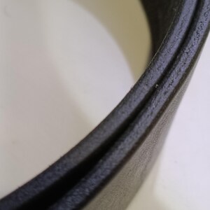 May include: Close-up of a black leather belt, highlighting the texture and construction. The belt appears to be made of a durable material, with a subtle sheen. The focus is on the edge and the layers of the belt.