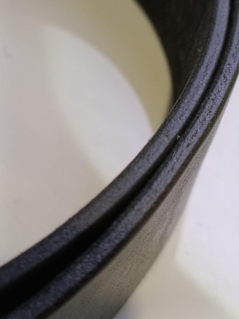 May include: Close-up of a black leather belt, highlighting the texture and construction. The belt appears to be made of a durable material, with a subtle sheen. The focus is on the edge and the layers of the belt.