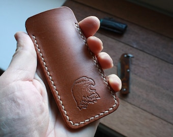 May include: A brown leather knife sheath with white stitching and an eagle design. 