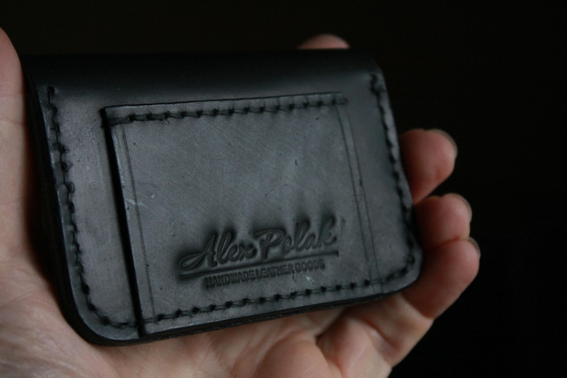 Puede incluir: Cartera de cuero negro con borde cosido y el texto "Alex Polak Handmade Leather Goods" grabado en relieve en la parte delantera.
