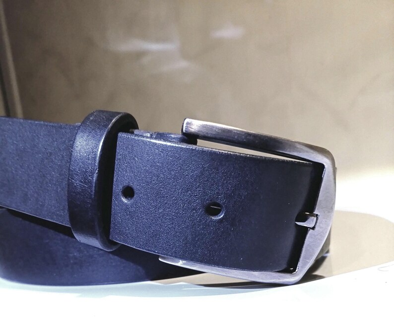 May include: Close-up of a black leather belt with a silver buckle. The belt is made of a smooth, dark material and features a classic design. The buckle is rectangular and has a brushed metal finish.
