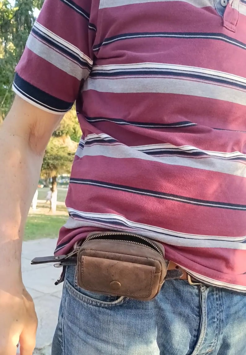 Peut inclure: Une petite pochette de ceinture en cuir marron dot&eacute;e d'un compartiment principal zipp&eacute; et d'une poche avant avec fermeture &agrave; bouton-pression. La pochette rectangulaire est fix&eacute;e &agrave; une ceinture et faite de cuir vieilli avec des coutures visibles.