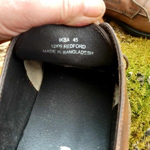 K&ouml;nnte beinhalten: Nahaufnahme des Innenraums eines braunen Lederschuhs. Die Innensohle ist schwarz und tr&auml;gt den Aufdruck "IKBA 45 12/09 REDFORD MADE IN BANGLADESH".