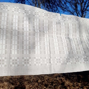 May include: A white linen tea towel with a gray checkered pattern hangs on a clothesline outdoors.