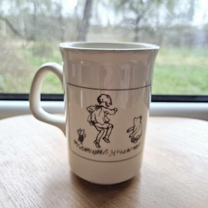 May include: White ceramic mug featuring a black and white illustration of a girl and a bear. The girl is jumping and the bear is standing on its hind legs. The text "When you wish upon a star..." is printed on the mug.