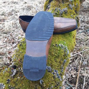 K&ouml;nnte beinhalten: Ein brauner Lederschuh mit einer schwarzen Gummisohle. Die Sohle tr&auml;gt den Schriftzug "IKON".